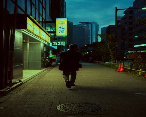 A man walking briskly down a city sidewalk during evening hours